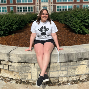 Student on stone wall in front of Geyer Hall sidewalks